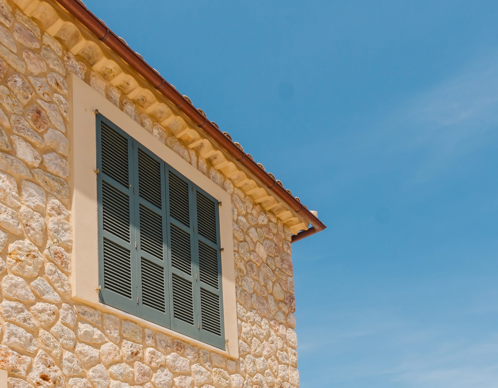 Ventana con persianas sobre fachada de piedra recién pintada con pintura de fachadas sostenible por pintores en Mallorca