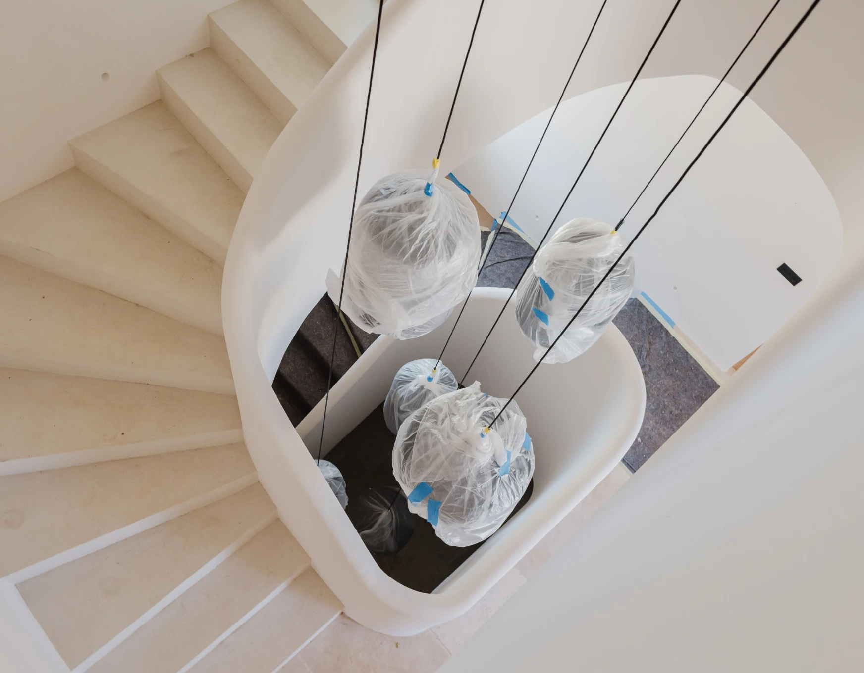 scalera de caracol e iluminación colgante protegida con plástico tras pintura de interiores por pintores en Mallorca de empresa de pintura Mallorca
